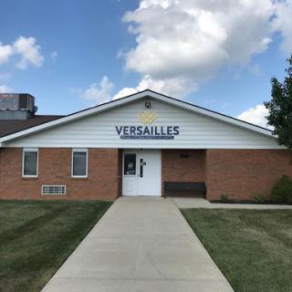 The Versailles building with a clear entrance path set against a partly cloudy sky.