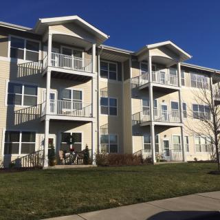 A modern three-story apartment building with balconies under a clear blue sky.