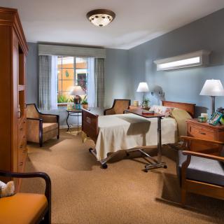 A well-furnished hospital room with a bed, chairs, and a window, providing a comfortable environment.