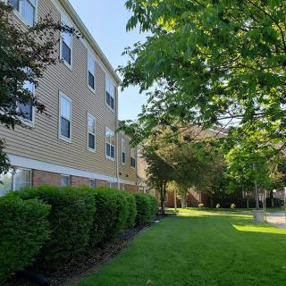 A quiet residential building surrounded by well-maintained greenery and a lush lawn on a sunny day.