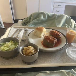 A hospital meal featuring meatballs, a side salad, a bread roll, and dessert.