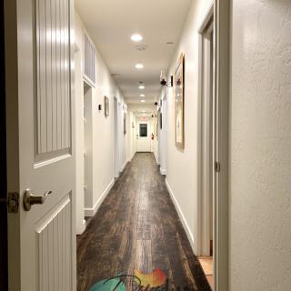A long, well-lit hallway with wooden floors and open doors on each side.