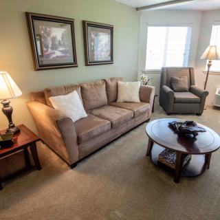 A cozy living room with a sofa, armchair, and coffee table, decorated with lamps and artwork on the walls.