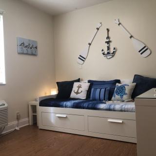 A cozy bedroom decorated with a nautical theme, featuring anchor and oar wall decor above a daybed adorned with blue and white pillows.