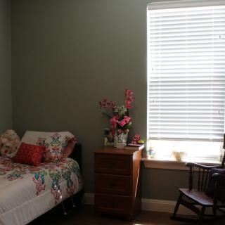 A cozy bedroom with a single bed, nightstand, and rocking chair bathed in sunlight.