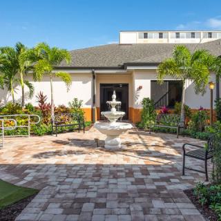 A serene garden with a central fountain surrounded by palm trees and benches in front of a building.