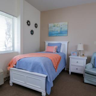 A cozy bedroom featuring a single bed with blue bedding and orange accents, complemented by a nightstand and armchair.