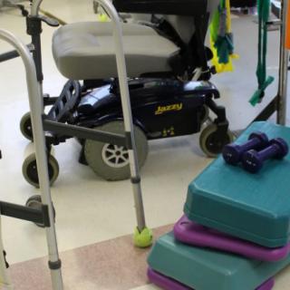 A physical therapy area with a wheelchair, walker, dumbbells, and step platforms.