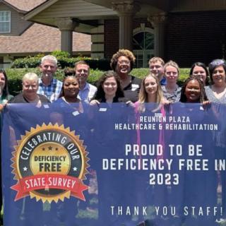 A group of healthcare staff celebrating a deficiency-free survey result in 2023, holding a banner outside.