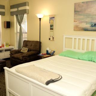A cozy bedroom with a bed, armchair, and floor lamp, enhanced by curtains and a wall painting.