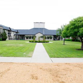 A well-maintained building with a large lawn and pathway leading to the entrance, surrounded by trees.