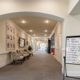 A well-lit hallway featuring a seating area, framed artwork on the walls, and a notice board.
