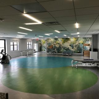 A spacious therapy room featuring a colorful mural and designated exercise areas.