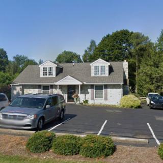 A suburban house with a parking lot and cars in front, surrounded by trees.