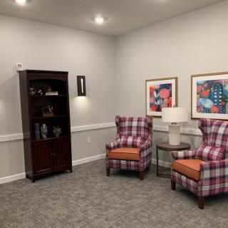 A cozy living room space with two plaid chairs, a wooden cabinet, and colorful artwork on the walls.
