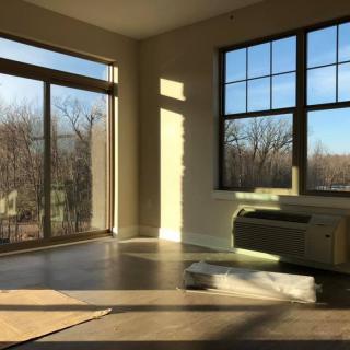 Sunlit empty room with large windows and a view of trees.