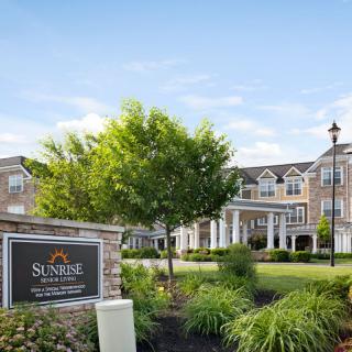 A large residential building surrounded by a well-maintained garden with a tree and a prominent sign in the foreground.