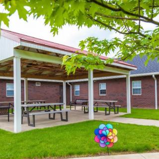 An outdoor pavilion with picnic tables surrounded by a grassy lawn and trees.