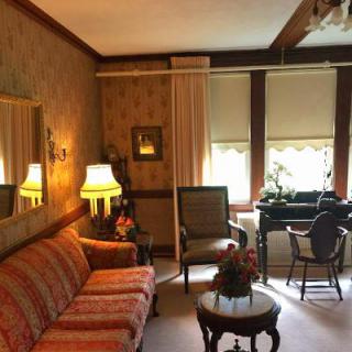 A cozy vintage living room featuring a patterned sofa, classic chairs, and warm lighting.
