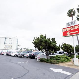 A hospital parking lot with an emergency sign pointing towards the entrance.