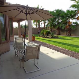 A sunny backyard patio with outdoor seating, umbrella, and a well-maintained garden.
