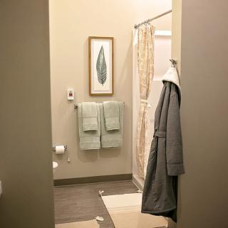 A bathroom interior featuring hanging towels, a robe, and framed artwork.