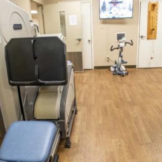 A gym room featuring exercise equipment, including an exercise bike and workout benches on a wooden floor.