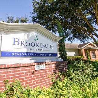 A sign for Brookdale Senior Living Solutions with surrounding landscaping and a building in the background.