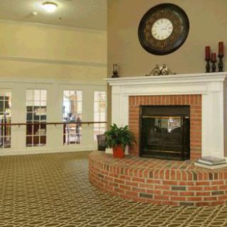 A cozy interior room featuring a brick fireplace, a decorative clock, and patterned carpet.