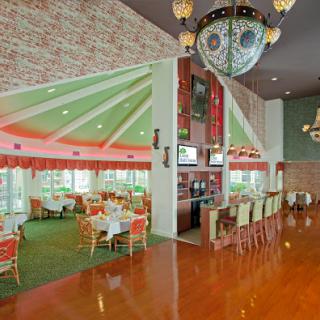 A vibrant restaurant interior featuring a modern design with a mix of green carpeting and elegant chandeliers.