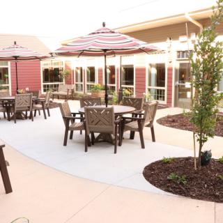 A well-maintained outdoor patio area featuring tables, chairs, and umbrellas surrounded by landscaping.