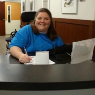 A woman smiling while writing at a desk in an office.