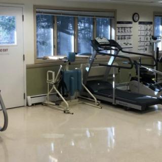 A fitness room equipped with exercise machines including a treadmill and other rehabilitation equipment.
