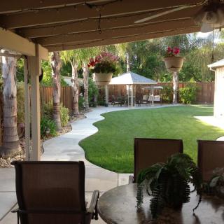 A peaceful backyard patio area with a neatly landscaped garden and lawn, featuring outdoor seating and hanging plants.