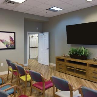 A modern waiting area with colorful chairs, a large television, and plant decorations.