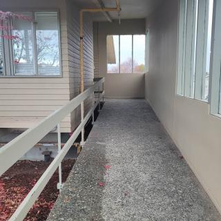 A covered outdoor hallway with windows on one side and a railing on the other.