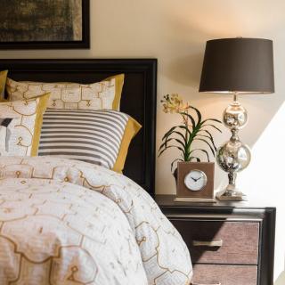 A cozy bedroom scene with a neatly made bed, decorative pillows, and a stylish nightstand featuring a lamp and clock.