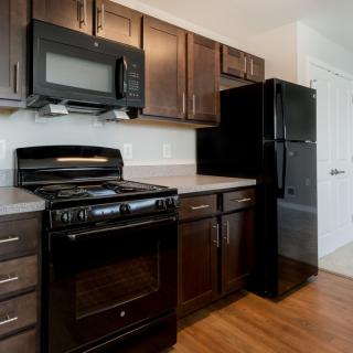 A modern kitchen featuring dark wood cabinets, a stove, microwave, and refrigerator.