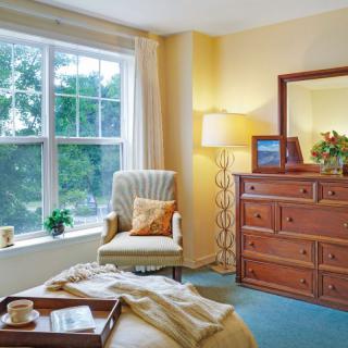 A cozy bedroom featuring a large window, comfortable armchair, and wooden dresser with a mirror.