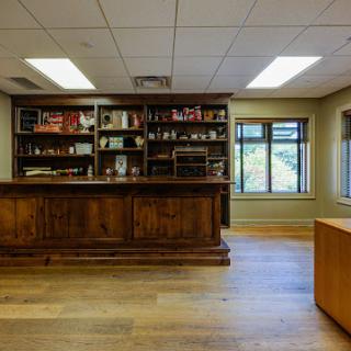 A modern office interior featuring a wooden reception desk, shelves filled with various items, and large windows allowing natural light.