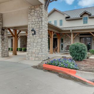 A stone building entrance with a landscaped garden and paved driveway.