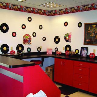 A retro-themed room with vinyl records on the walls, red cabinets, and a black countertop.