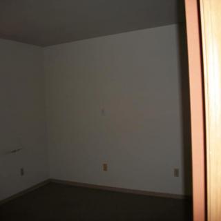 An empty room with white walls, carpeted floor, and a partially open doorway.