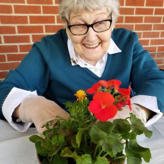 An elderly woman smiles while tending to flowers indoors.