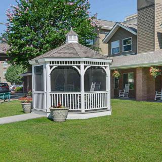 A white gazebo stands on a well-maintained lawn in front of a building.