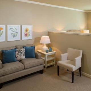 A cozy living room with a sofa, armchair, table lamp, and wall art.
