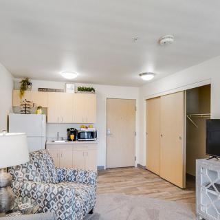 A modern apartment interior featuring a cozy living room with patterned furniture and a compact kitchenette.