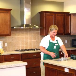 A woman prepares food in a modern kitchen, showcasing the warm tones of cabinetry and a clean workspace.