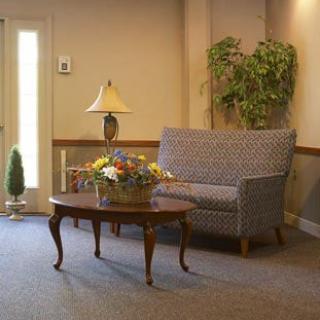 A cozy waiting room with a sofa, coffee table, lamp, and plant decor.