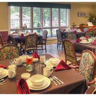 A well-set dining room with tables adorned with fine tableware and red napkins, facing large windows.